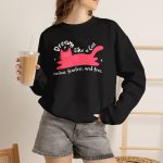Person wearing a crewneck sweatshirt with a pink reclining cat with a raised tail, round eyes and white sparkles printed on the front