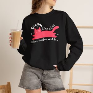 Person wearing a crewneck sweatshirt with a pink reclining cat with a raised tail, round eyes and white sparkles printed on the front