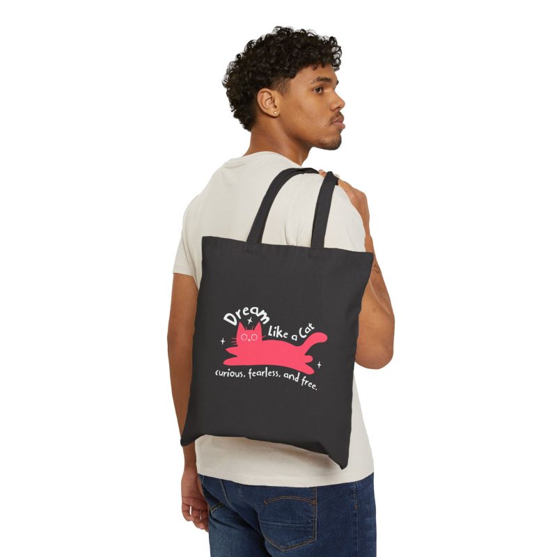 Person carrying a black canvas tote with a pink reclining cat with a raised tail, round eyes and white sparkles facing outward
