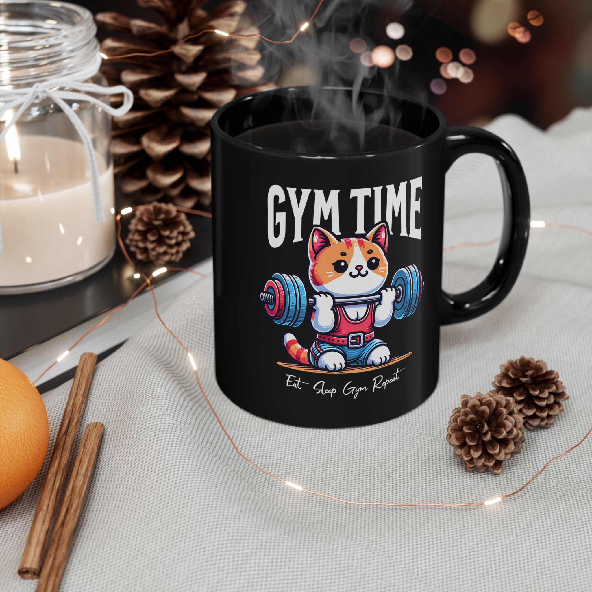 Glossy black ceramic mug showing an orange-and-white kitten lifting a barbell with blue and pink weight plates