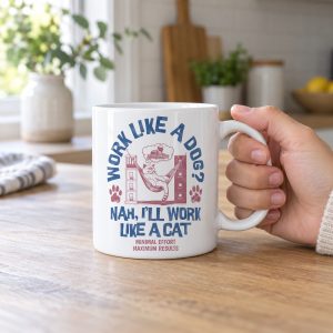 Person holding a white ceramic mug showing a cat reclining in a hammock between filing cabinets with blue lettering and red paw prints
