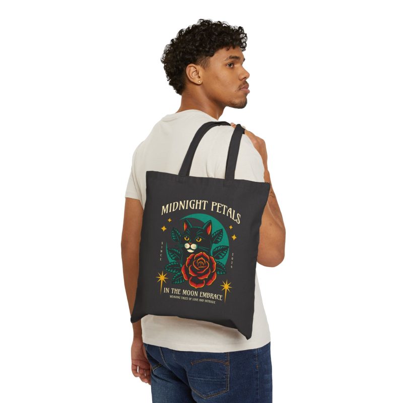 Person carrying a black canvas tote with the black cat with a red rose and golden stars graphic facing outward