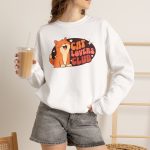 Person wearing a crewneck sweatshirt with a smiling orange tabby beside retro lettering in an oval badge with hearts and starbursts printed on the front