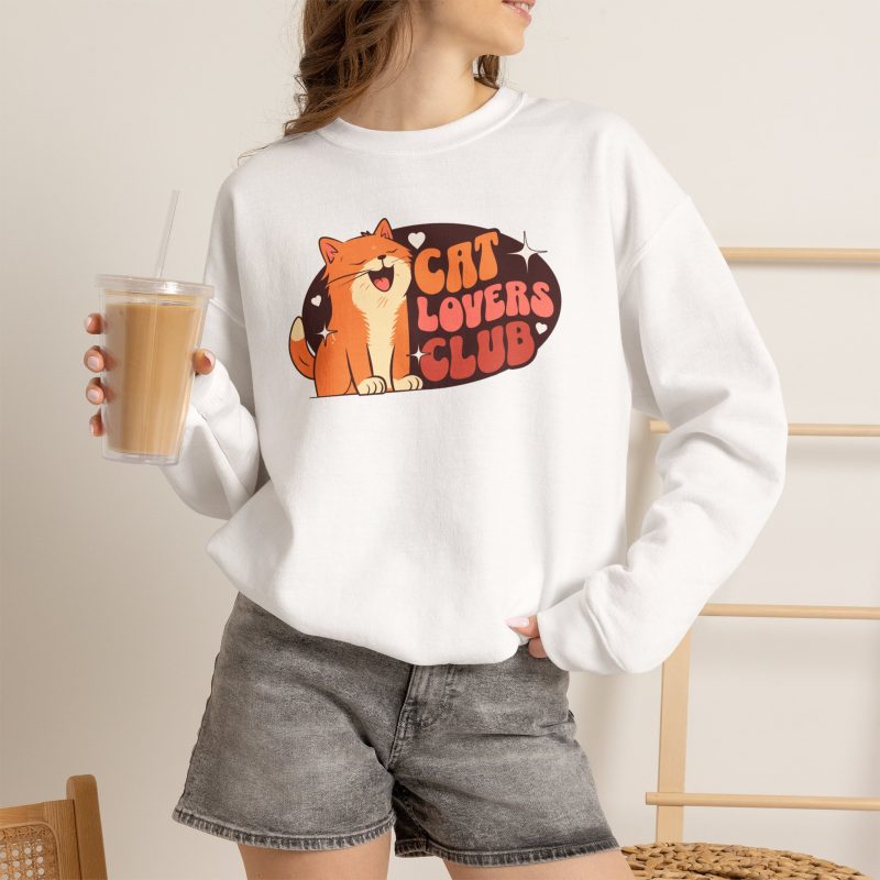Person wearing a crewneck sweatshirt with a smiling orange tabby beside retro lettering in an oval badge with hearts and starbursts printed on the front