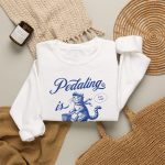 A blue tabby riding a bicycle with a basket with Pedaling is Purr-sonal lettering