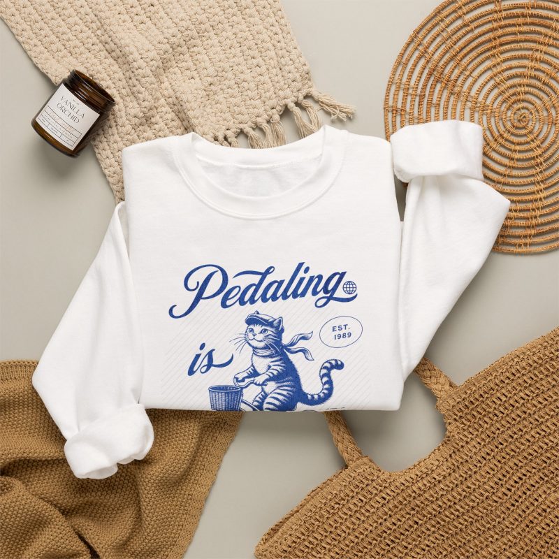 A blue tabby riding a bicycle with a basket with Pedaling is Purr-sonal lettering