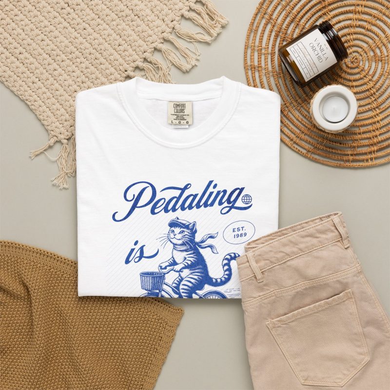 A blue tabby riding a bicycle with a basket with Pedaling is Purr-sonal lettering