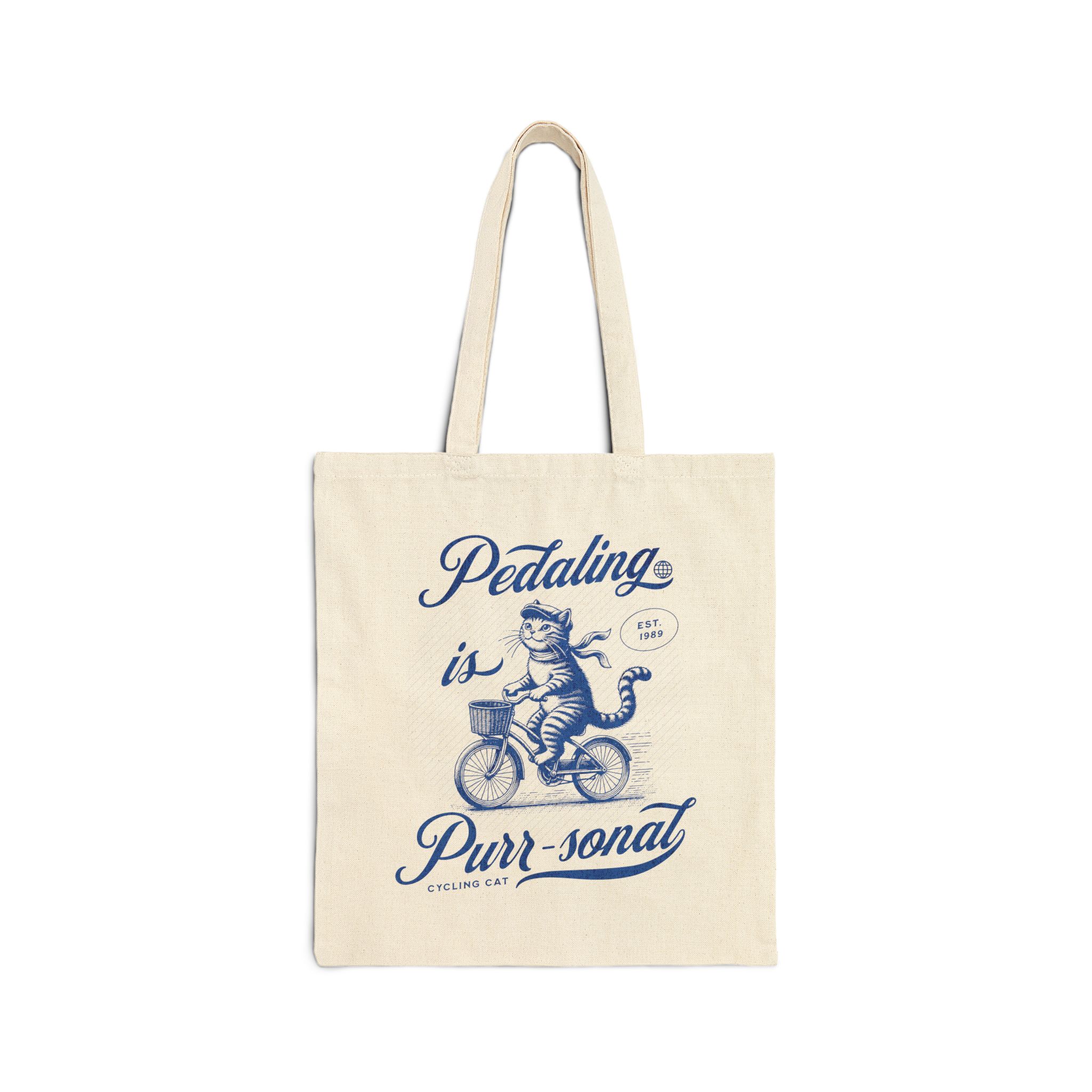 A blue tabby riding a bicycle with a basket printed on the front of a natural canvas tote