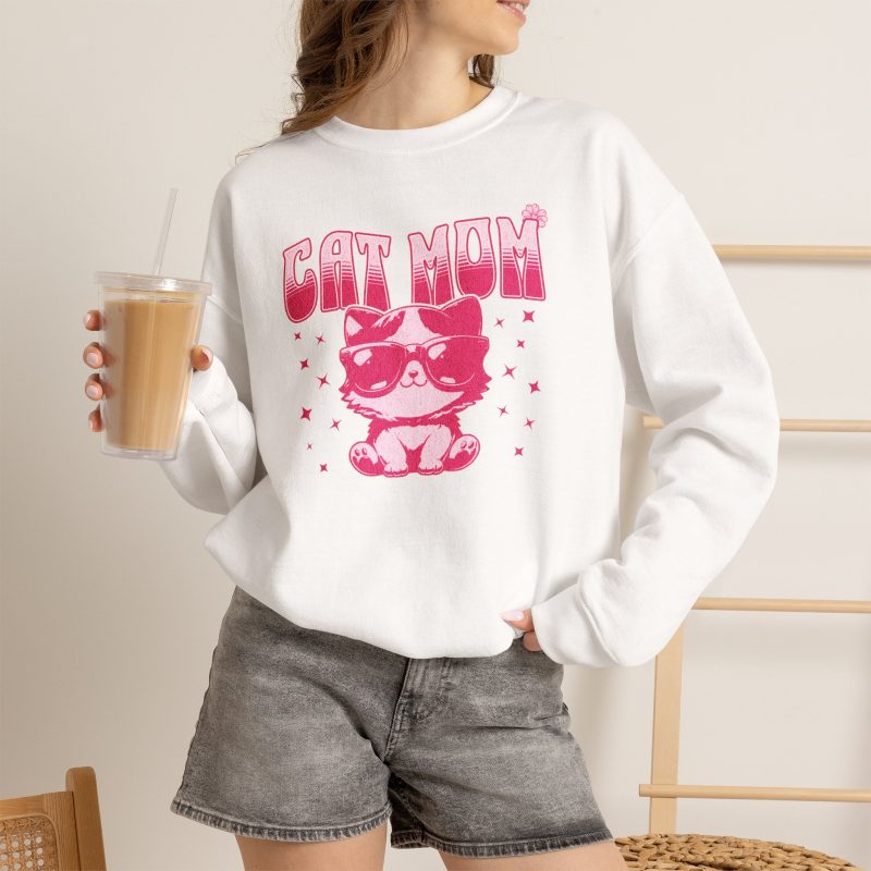 Person wearing a crewneck sweatshirt with a seated kitten in oversized sunglasses with pink striped lettering and stars printed on the front