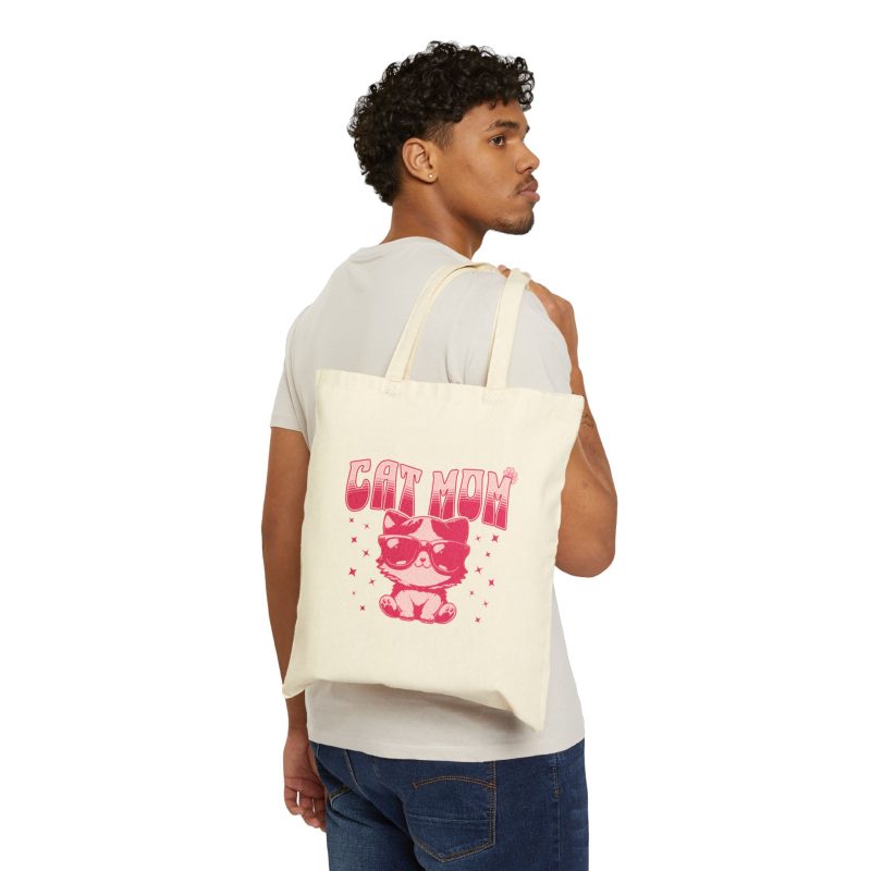 Person carrying a natural canvas tote with a seated kitten in oversized sunglasses with pink striped lettering and stars facing outward