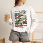 Person wearing a crewneck sweatshirt with a Santa-hat kitten with holly and an ornament graphic on the front