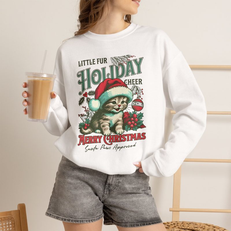 Person wearing a crewneck sweatshirt with a Santa-hat kitten with holly and an ornament graphic on the front