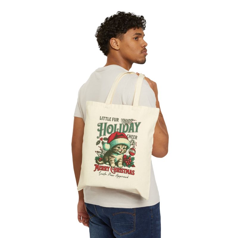 Person carrying a natural canvas tote with the Santa-hat kitten with holly and an ornament graphic facing outward