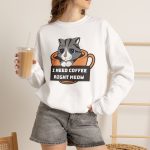 Person wearing a crewneck sweatshirt with a gray tabby in an orange coffee cup graphic on the front