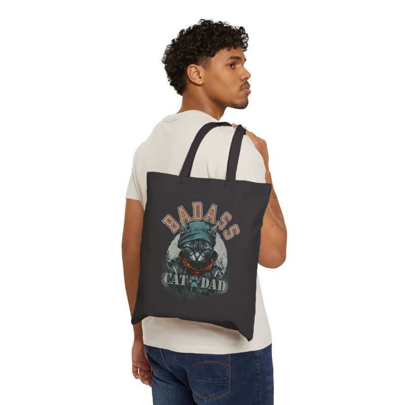 Person carrying a black canvas tote with the tabby in a cap, jacket and scarf graphic facing outward