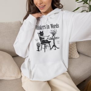 Person wearing a hoodie with a cat reading a book at a café table graphic on the front