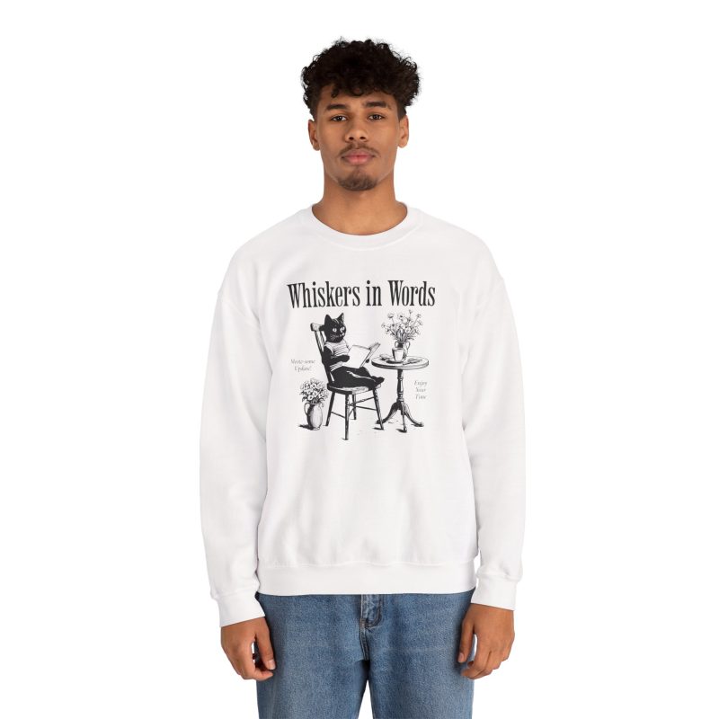 Person wearing a crewneck sweatshirt with a cat reading a book at a café table graphic on the front