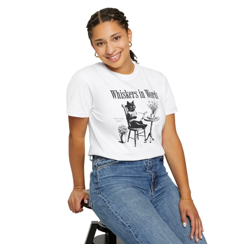 Person wearing a tee with a cat reading a book at a café table graphic on the front