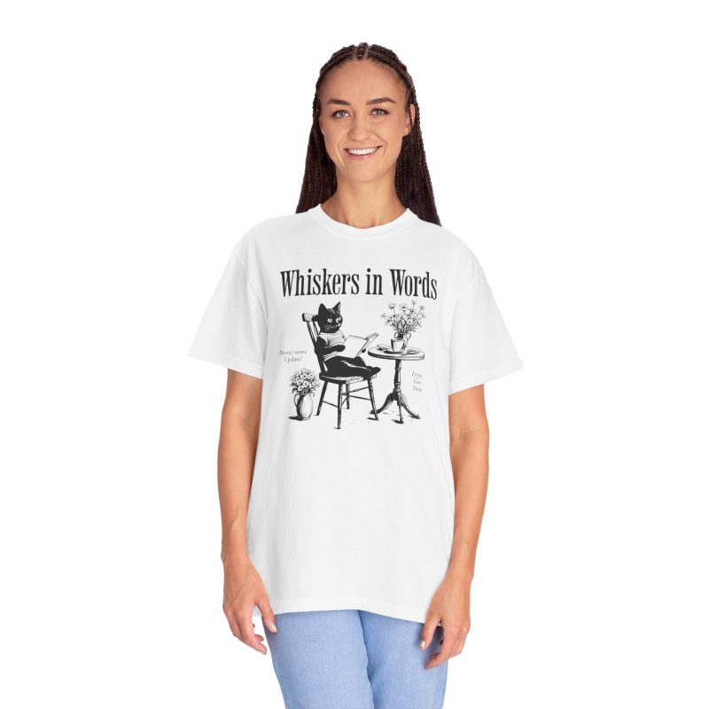 Person wearing a tee with a cat reading a book at a café table graphic on the front