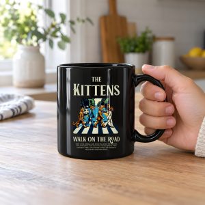 Person holding a glossy black ceramic mug with crosswalk kittens