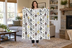 A woman holding open a white cat butt pattern flannel blanket in a bright living room.